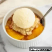 Grandma's Classic Peach Cobbler 6 A white ramekin on a marble surface filled with peach cobbler and a scoop of ice cream on top.