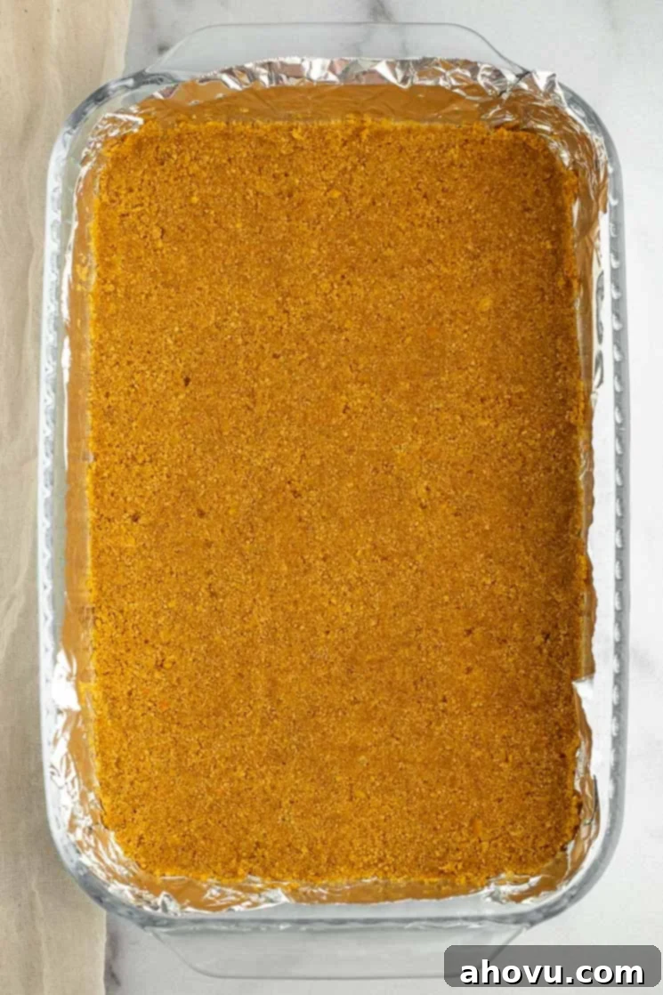 Irresistible Magic Bars 3 A 9x13 inch baking pan meticulously lined with aluminum foil, featuring a perfectly pressed graham cracker crust as the base for Magic Cookie Bars.