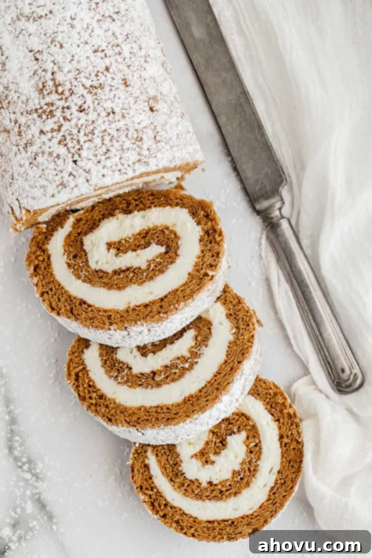 Autumn Spice Swirl 2 A partially sliced pumpkin roll on a marble surface, revealing its beautiful spiral of cake and cream cheese filling.