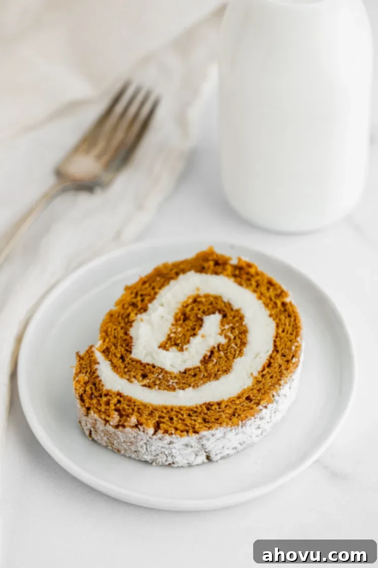 Autumn Spice Swirl 3 A beautifully sliced piece of pumpkin cream cheese roll resting on a pristine white plate, showcasing the delicate orange cake and white frosting swirl.