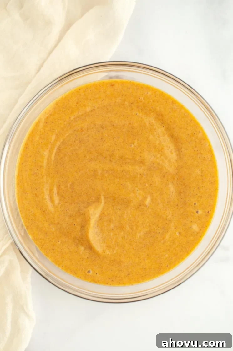 Autumn Spice Swirl 4 A clear glass bowl showcasing a vibrant orange pumpkin cake batter, perfectly smooth and ready for baking.