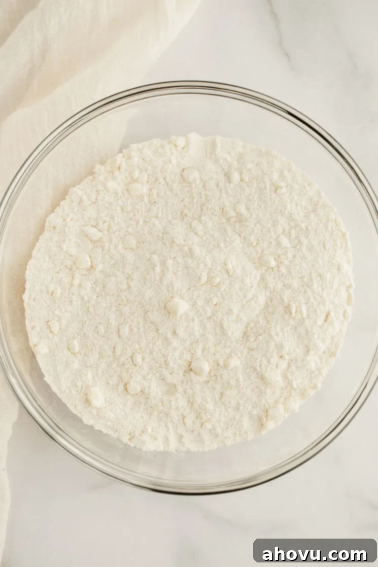 A pristine glass bowl containing a perfectly mixed blend of dry ingredients – all-purpose flour, granulated sugar, baking powder, and salt – ready for making scones.