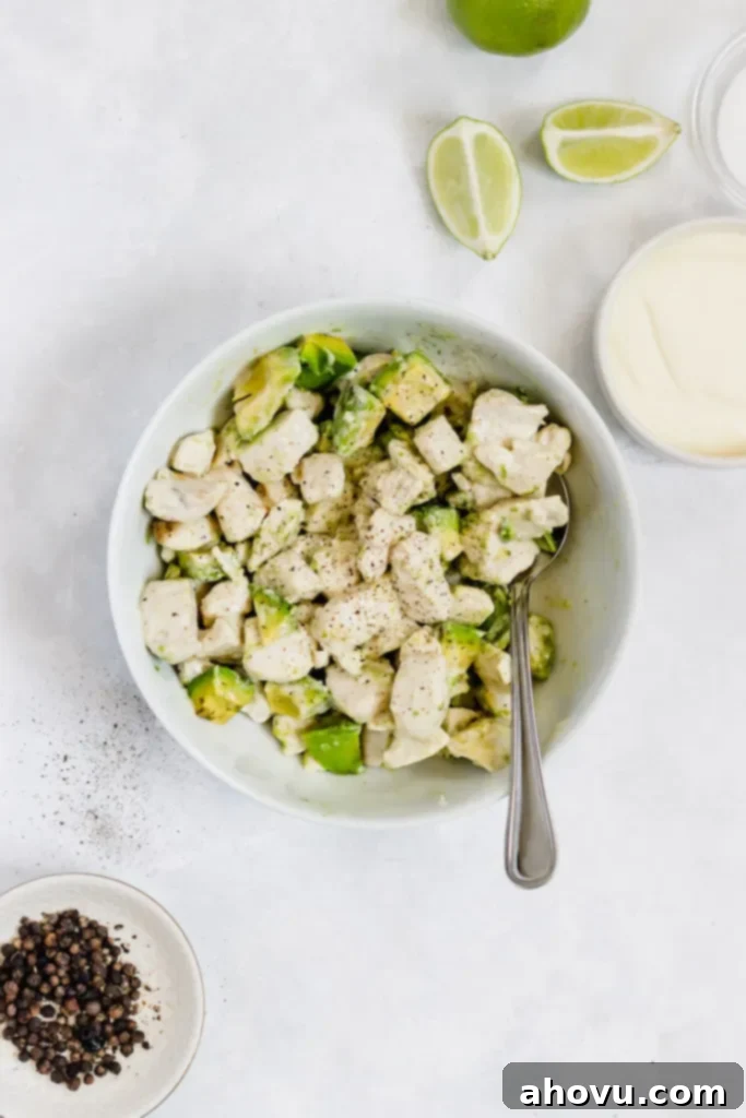 Avocado chicken salad in a white bowl. A small bowl of mayo and sliced limes are laying beside the bowl.
