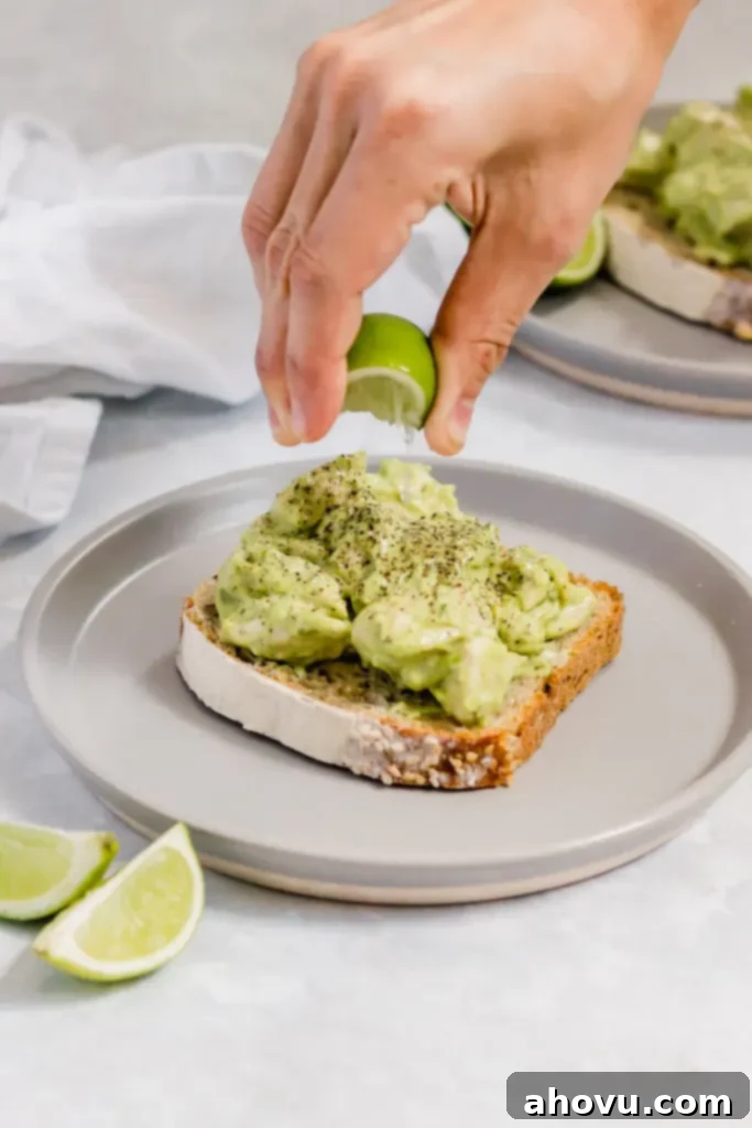 A slice of bread topped with avocado chicken salad. Fresh lime juice is being squeezed on top of it.