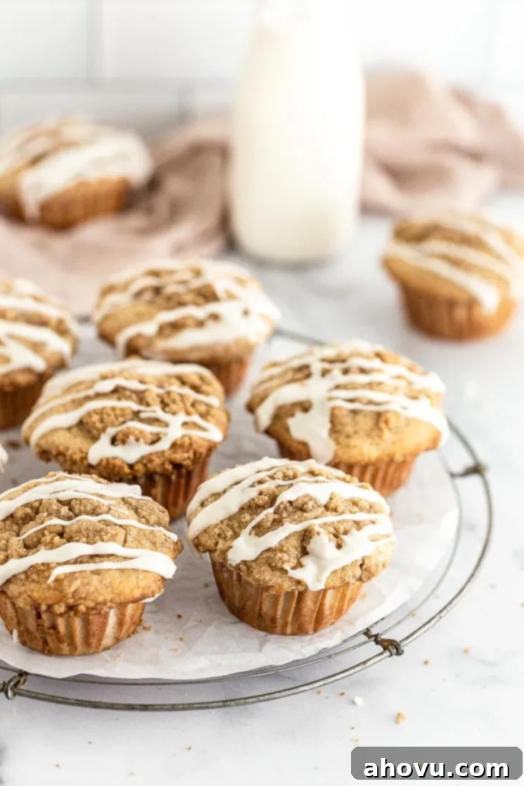 Spiced Apple Muffins 3 Glazed apple muffins on top of a round wire rack, showcasing the sweet drizzle over the golden tops.