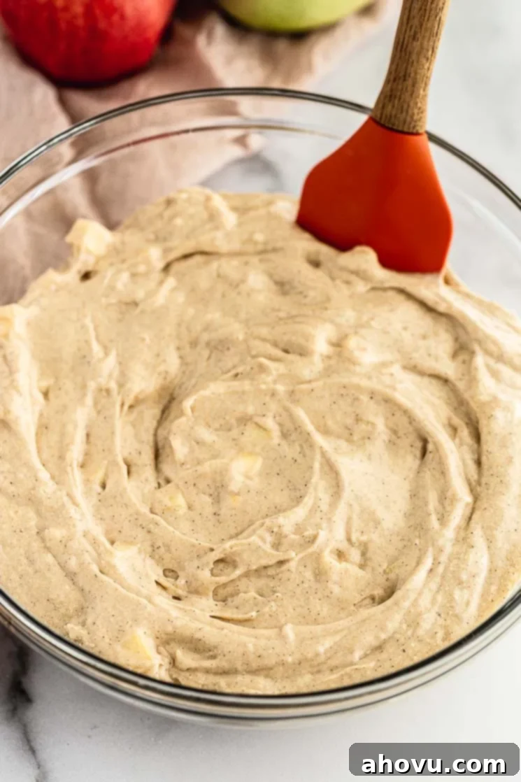 Spiced Apple Muffins 4 A picture of muffin batter, thick and luscious, inside of a clear glass mixing bowl, with small apple pieces visible.