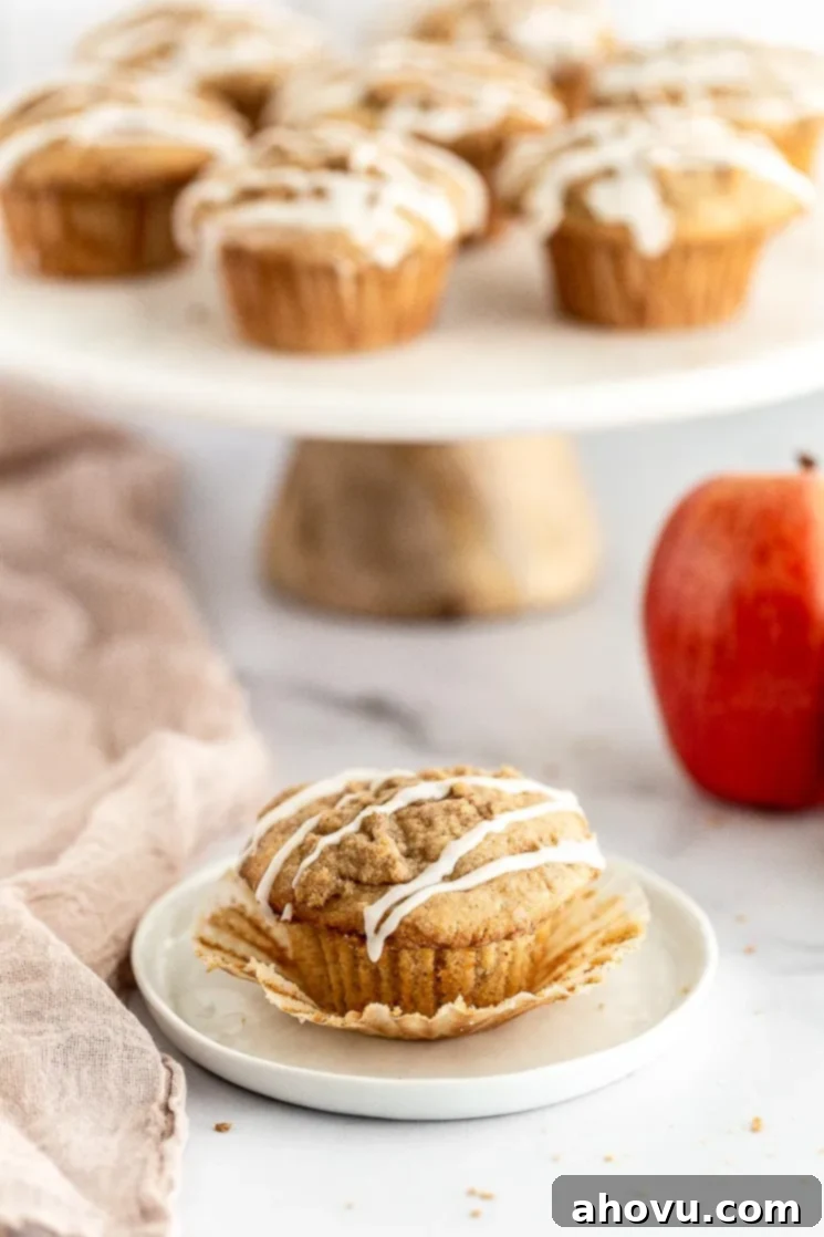 Spiced Apple Muffins 6 A close-up of an apple muffin on a white plate with the paper liner peeled away, revealing its tender, apple-filled interior.