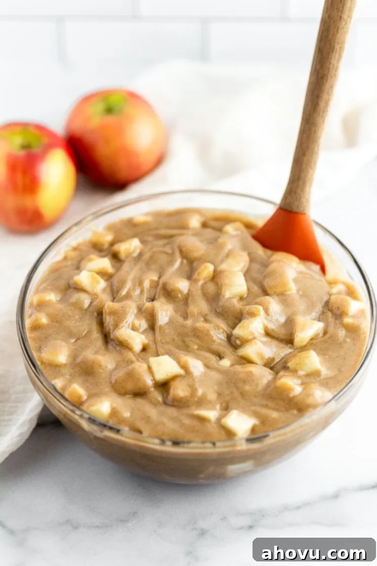 Orchard Apple Delight 3 A glass bowl filled with cake batter and freshly chopped apples, ready for baking.