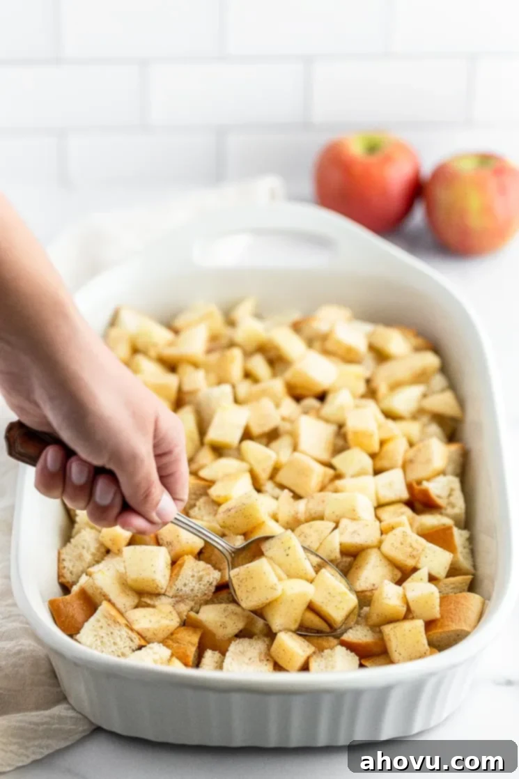 Chopped apples being added on top of cubed bread in a baking pan, ready for the next layer of the French toast casserole.