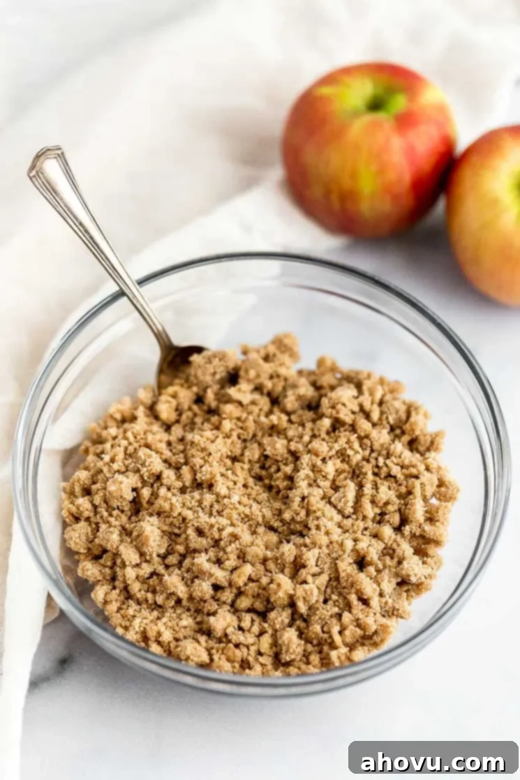 A bowl filled with streusel topping, with fresh apples in the background, ready to be added to the casserole.