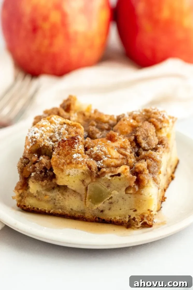 A slice of apple French toast casserole topped with maple syrup on a white plate, ready for a delicious breakfast spread.