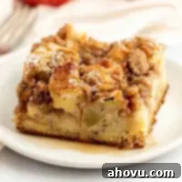 A slice of apple streusel French toast casserole topped with pure maple syrup on a white plate, showcasing the crispy streusel.