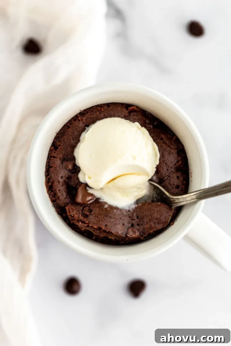 A delightful chocolate mug cake, topped with a melting scoop of vanilla ice cream, with a spoonful already taken, revealing its moist and rich interior.