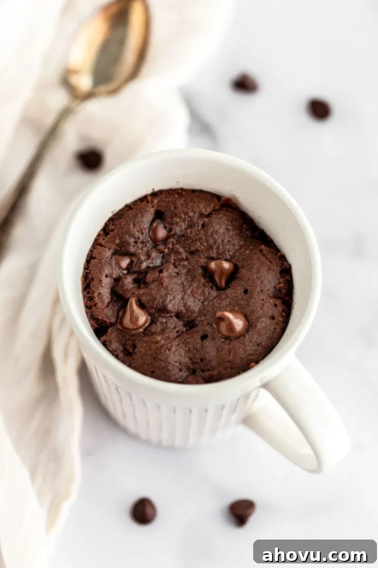 A freshly microwaved chocolate mug cake, still steaming slightly, sitting on a pristine marble surface, indicating its readiness for delicious toppings.