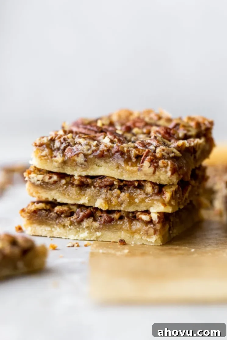 A stack of three golden brown pecan pie bars on rustic brown parchment paper, showcasing the nutty topping and shortbread crust.