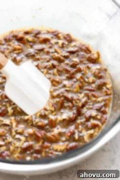 A glass mixing bowl filled with the rich, amber-colored pecan pie filling, ready to be poured.