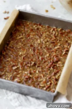 The glossy pecan pie filling evenly spread over the pre-baked shortbread crust in a baking pan.
