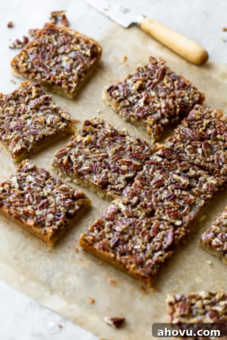 Beautifully arranged finished pecan pie bars on parchment paper, with a knife in the soft background, ready for serving.