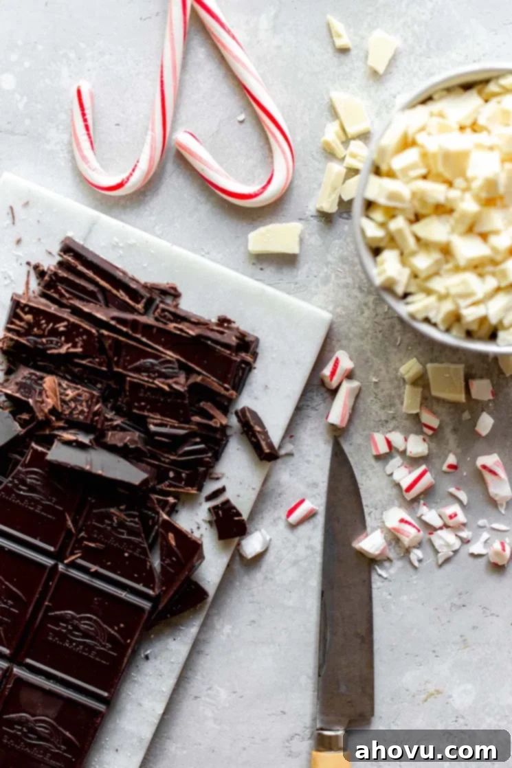 A collection of ingredients for making peppermint bark, including chocolate bars, peppermint extract, oil, and candy canes, arranged on a neutral gray surface.