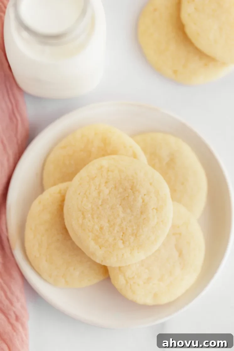 A white plate filled with perfectly baked, soft and chewy no-chill sugar cookies, with more cookies and a jug of fresh milk in the background, ready for serving.