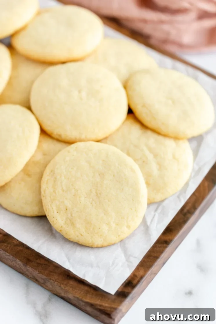 A rustic wooden board abundantly covered with stacks of golden-brown, soft, and chewy easy sugar cookies, ready to be enjoyed or shared.
