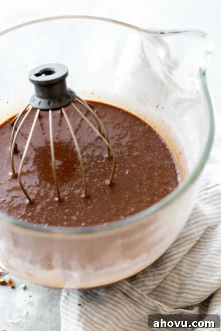 Coconut Pecan Chocolate Dream 3 A glass mixing bowl filled with rich chocolate cake batter, with a whisk resting in the bowl, ready for the next step.
