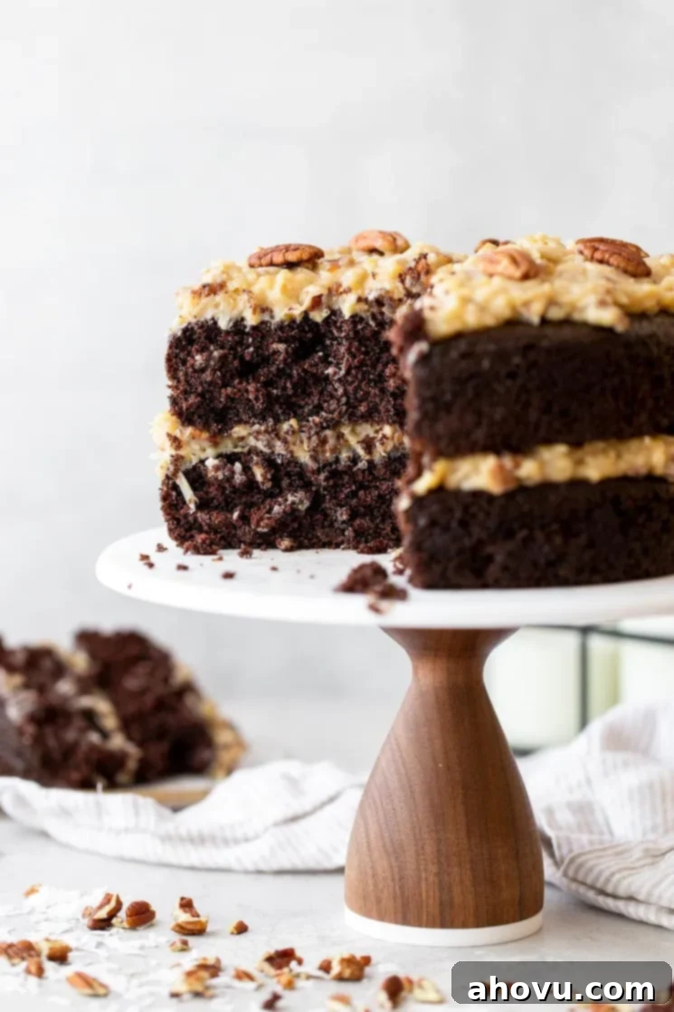 Coconut Pecan Chocolate Dream 5 A stunning layered German Chocolate Cake on a marble cake stand, with a slice removed to reveal its moist chocolate layers and generous coconut pecan frosting. Ready to be enjoyed.