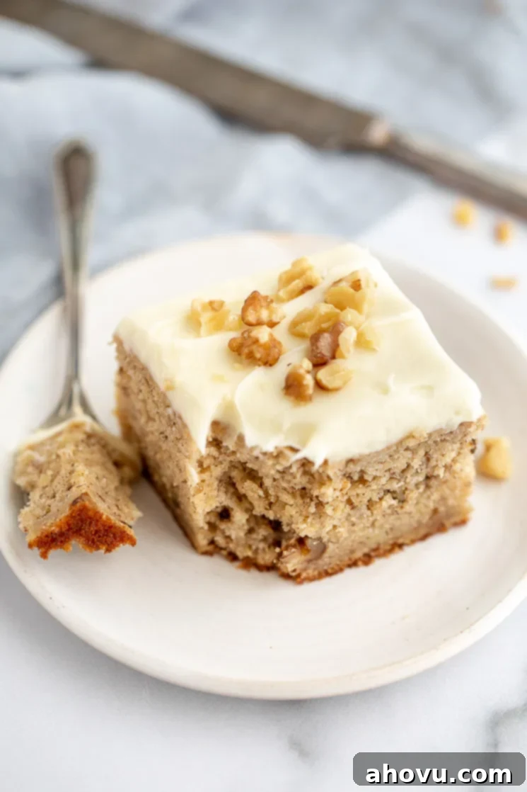 Banana Cake 2 A square piece of banana cake topped with cream cheese frosting and extra walnuts that has a bite sized piece taken out on an antique fork. This moist banana cake is perfect for using overripe bananas.