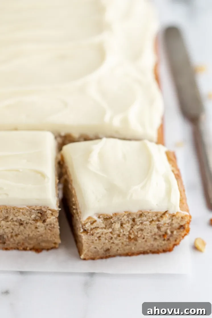 Banana Cake 6 A finished banana cake, resting on a marble surface, with one piece cut and pulled away to show the texture of the cake. A slice of moist banana cake with cream cheese frosting, showing off its perfect texture.