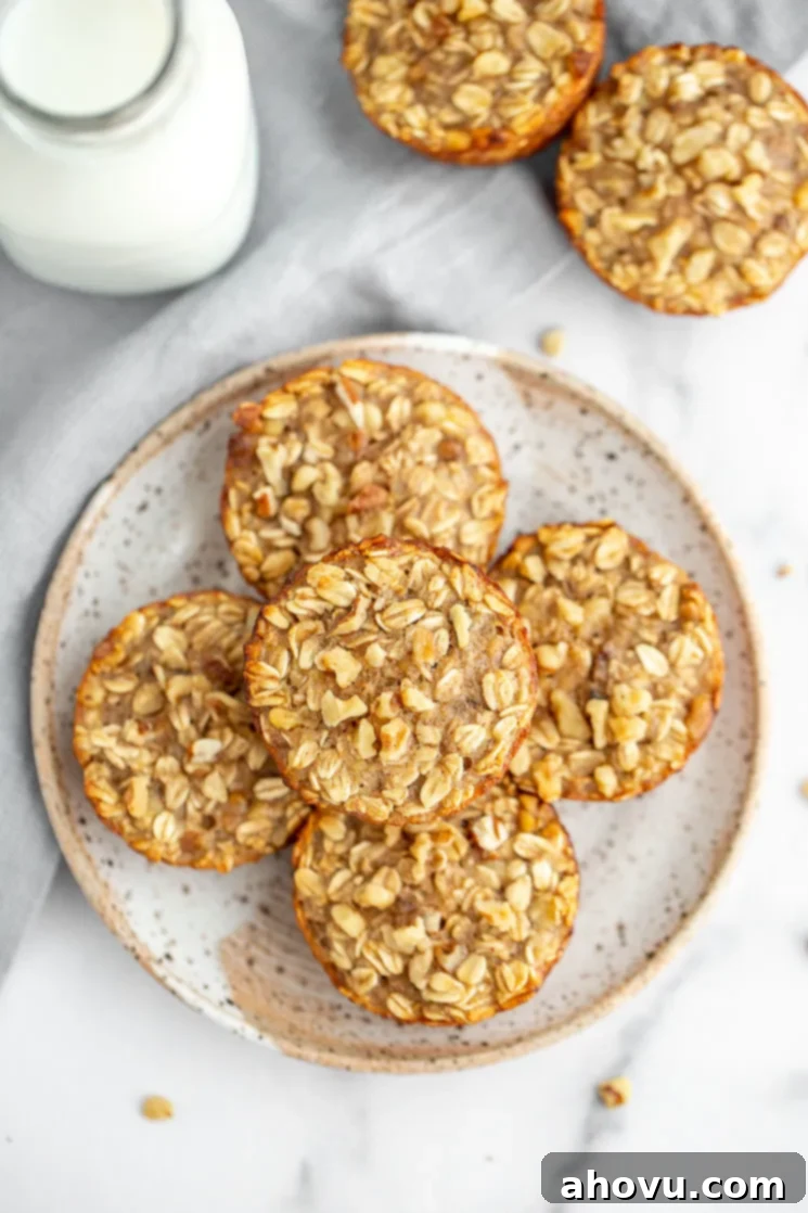 A speckled plate holding two banana baked oatmeal cups, with more cups and a glass of milk in the background, set on a marble surface.