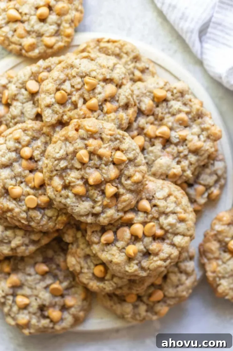 A stack of oatmeal scotchies on a rustic clay plate with a striped napkin in the background. 