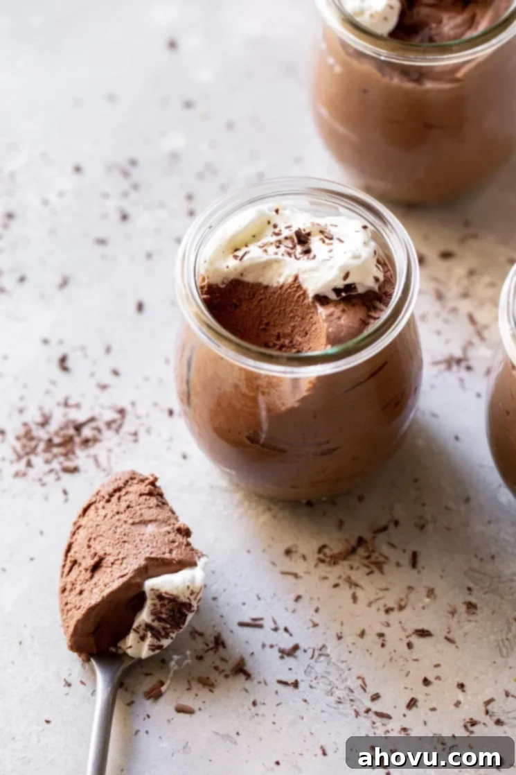 Three small jars filled with chocolate mousse topped with whipped cream and chocolate shavings.