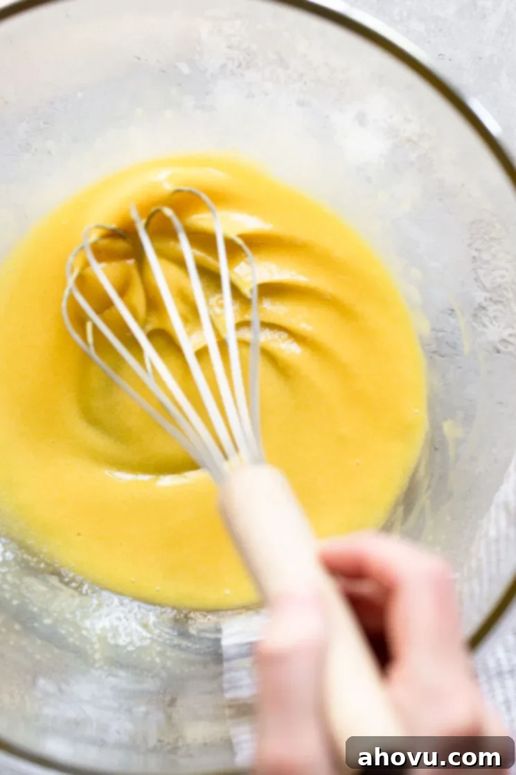 A glass bowl with eggs and sugar being mixed together with a whisk.