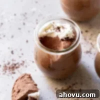 A glass jar filled with chocolate mousse topped with whipped cream and chocolate shaving with a spoonful taken out to show texture.