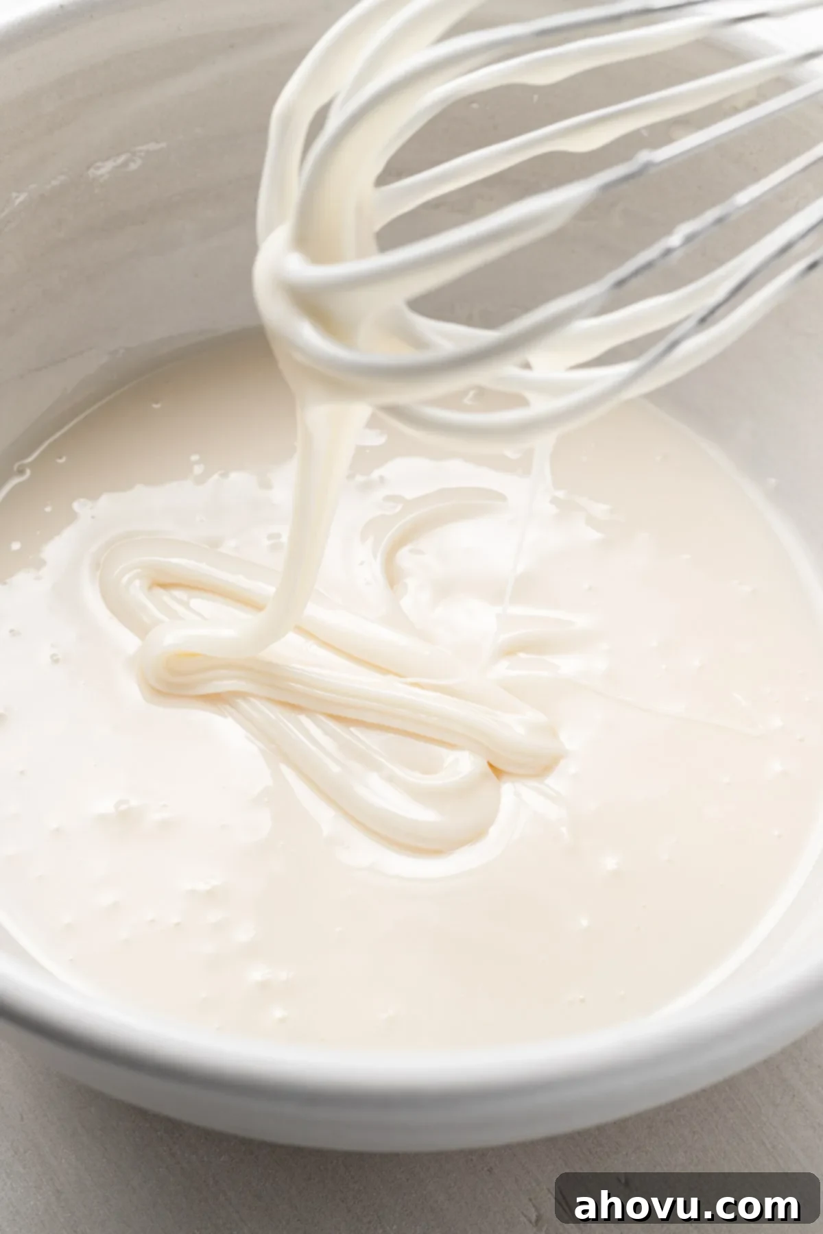 A bowl of sugar cookie icing with a whisk held over it to show the outline consistency.