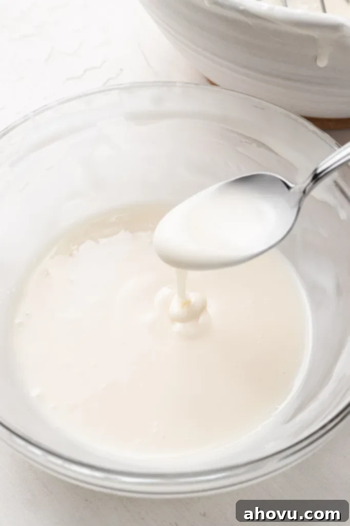 A glass mixing bowl of flood icing with a spoon held aloft. 