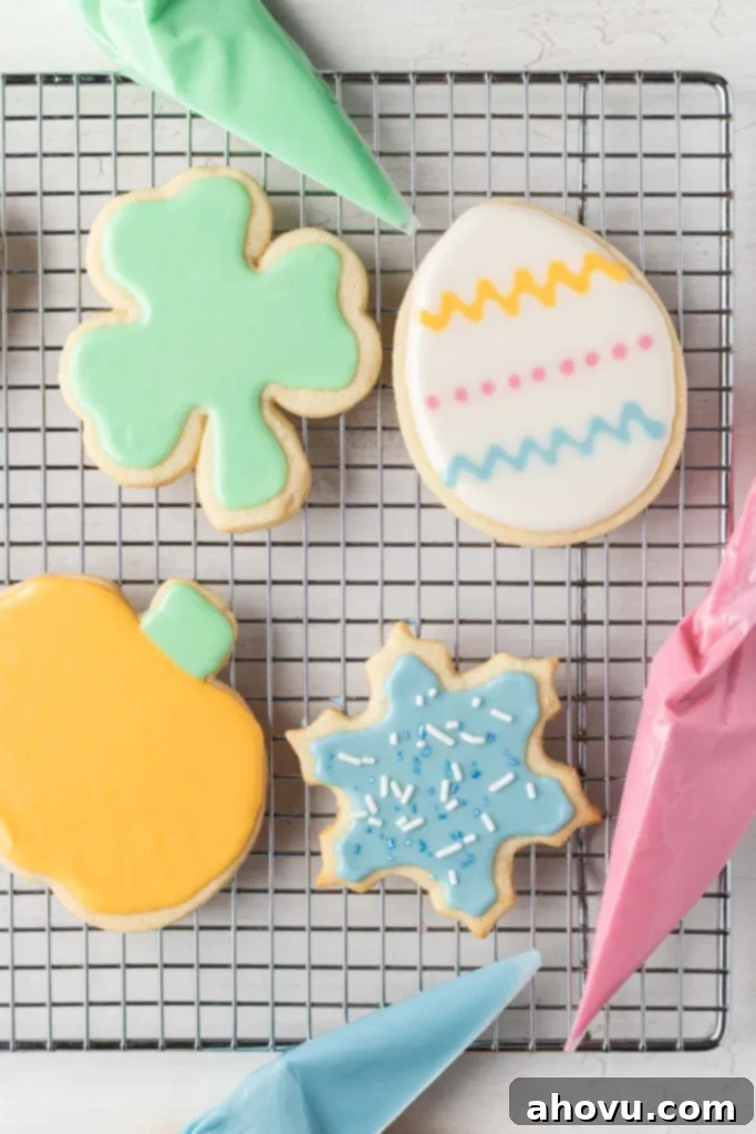 An overhead view of four iced sugar cookies on a wire cooling rack. Three piping bags filled with icing surround the cookies. 