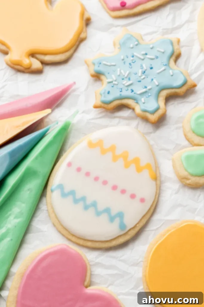 Piping bags of colored icing and iced sugar cookies on white parchment paper. 