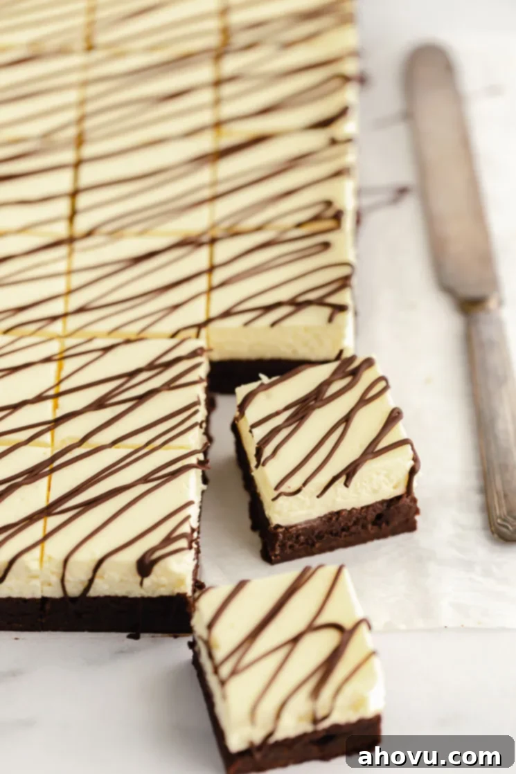 A sheet of parchment paper with cheesecake brownies cut into individual servings and two pulled out to show the layer details.