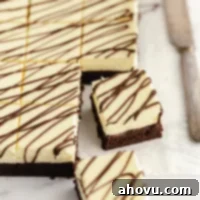 Sliced cheesecake brownies drizzled with melted chocolate on a piece of parchment paper.