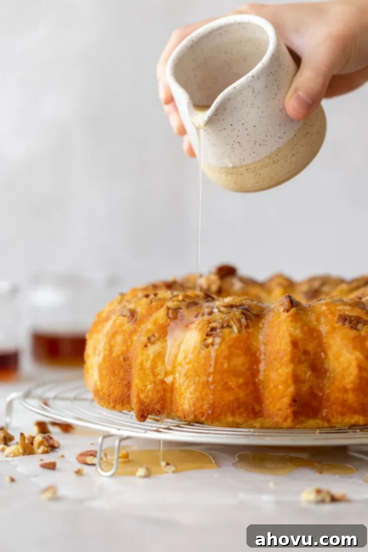 A baked rum cake resting on a round cooling rack and the rum glaze being poured over the top.