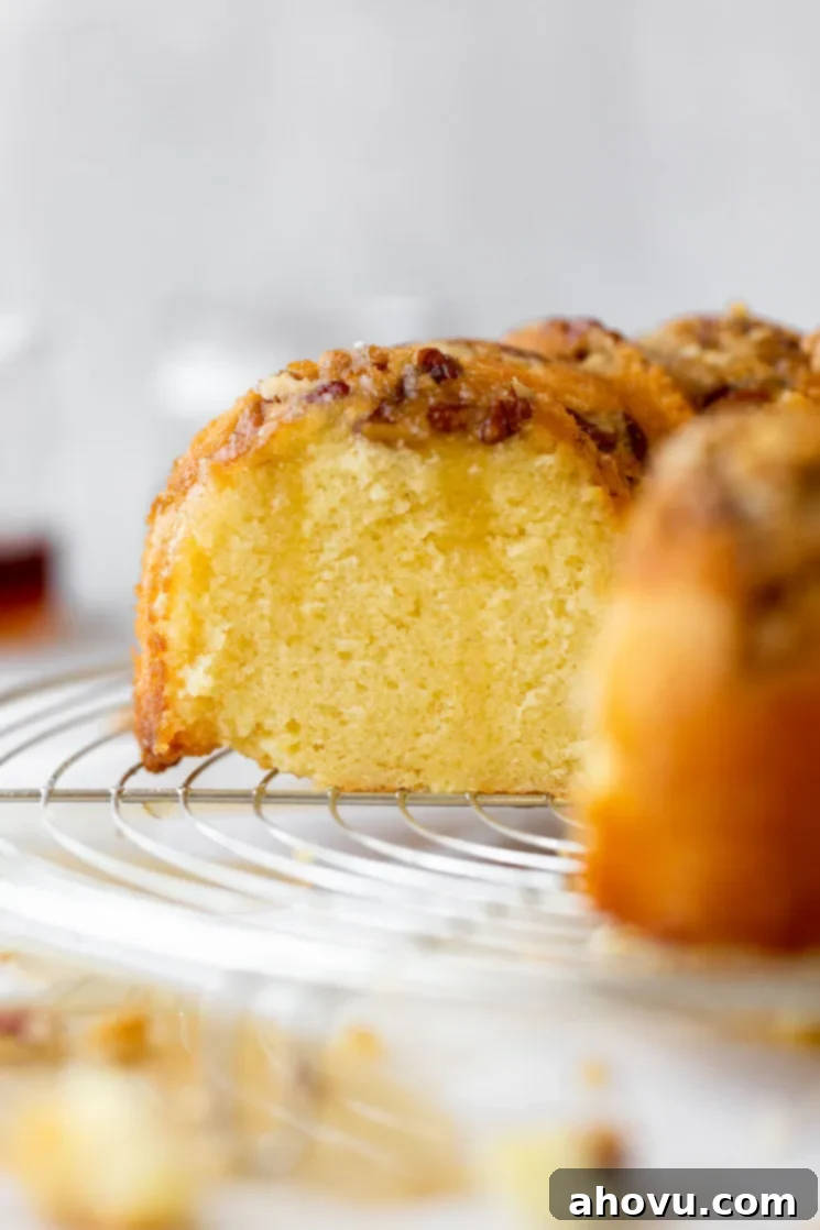 A finished rum cake resting on a round cooling rack with a slice cut out to show the cake texture.