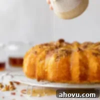 A baked rum cake resting on a round cooling rack and the rum glaze being poured over the top.