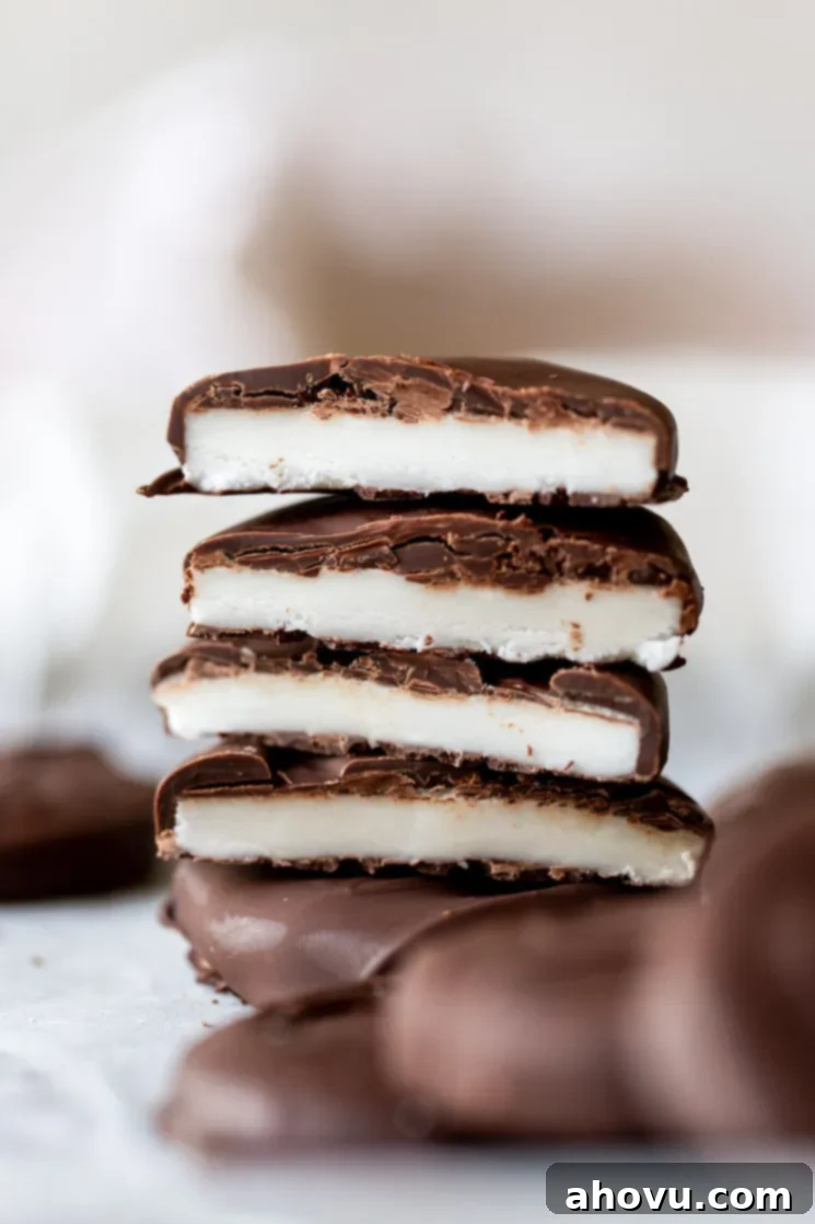 A stack of perfectly cut homemade peppermint patties, revealing their distinct creamy white peppermint filling and a decadent chocolate coating. The image showcases the smooth texture of the mint center and the glossy finish of the chocolate shell.