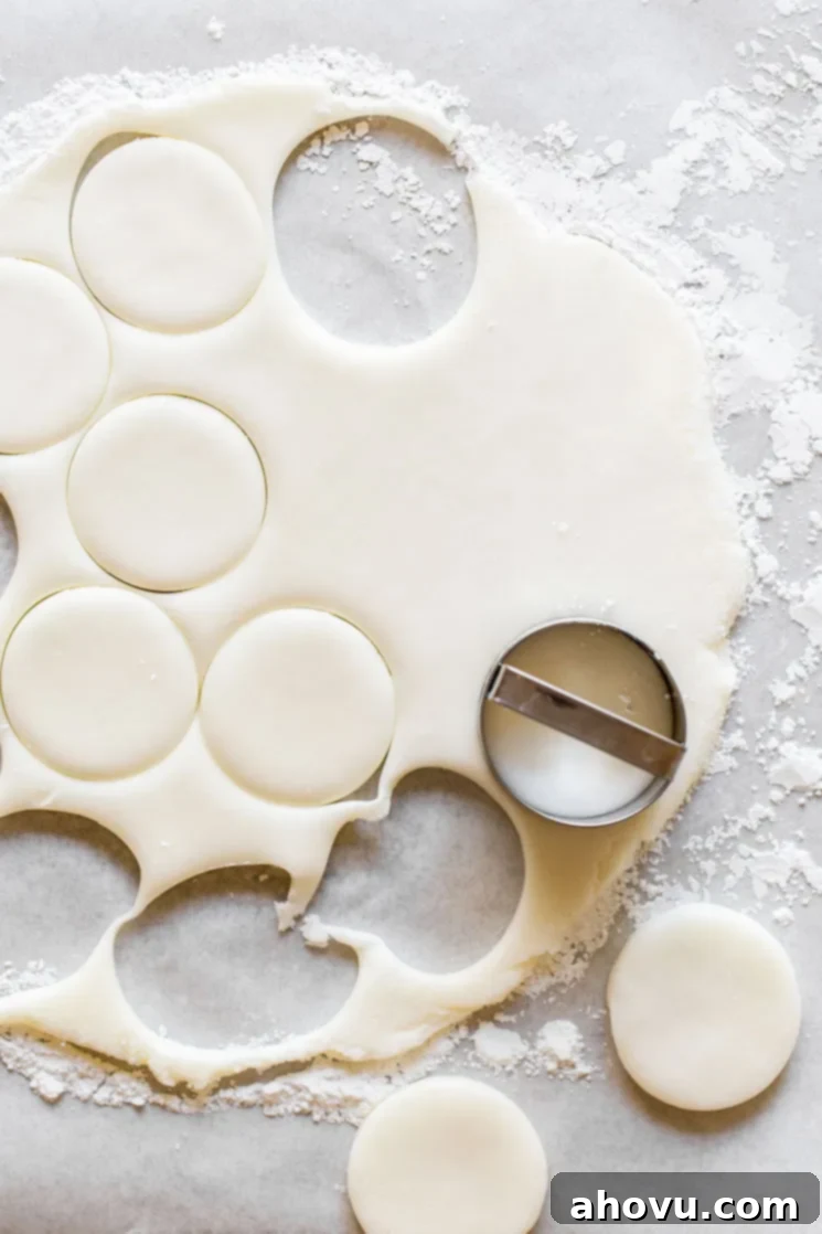 Peppermint patty dough, rolled thinly between two sheets of parchment paper, with perfect circles being cut out using a small round cookie cutter. The surface is lightly dusted with powdered sugar.