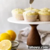 A marble cake stand with lemon poppy seed muffins being topped with a lemon glaze.