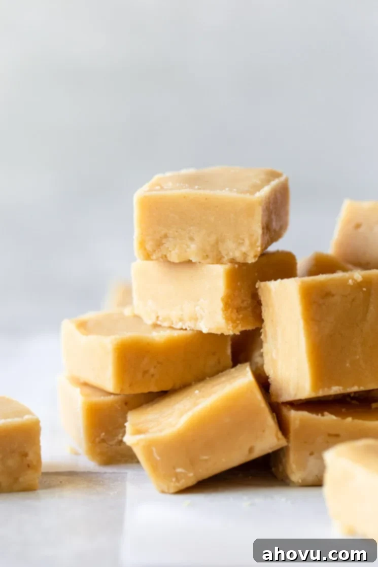Pieces of peanut butter fudge stacked on a gray surface lined with parchment paper, showcasing its smooth texture.