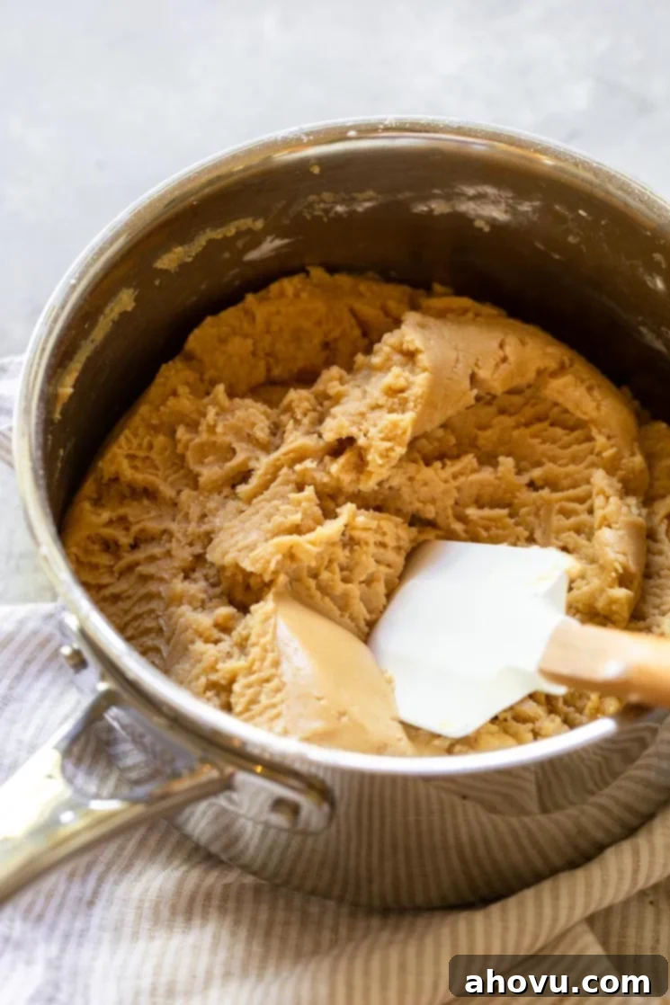 Peanut butter fudge mixture being stirred in a saucepan on the stove, showing its smooth, melted consistency.