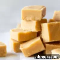 Pieces of Peanut Butter Fudge stacked on a gray surface and parchment paper.