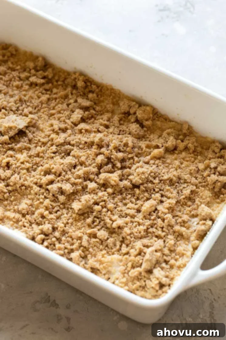 A white baking pan filled with cake batter and topped with a streusel topping, ready for the oven.
